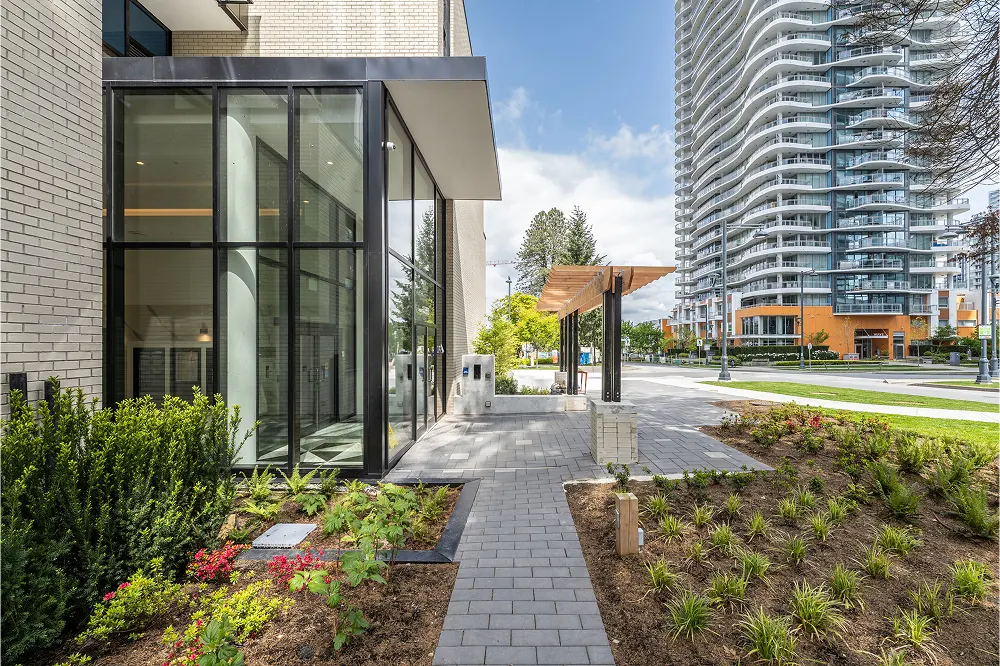 Paver walkway with planted beds beside a glass building entrance