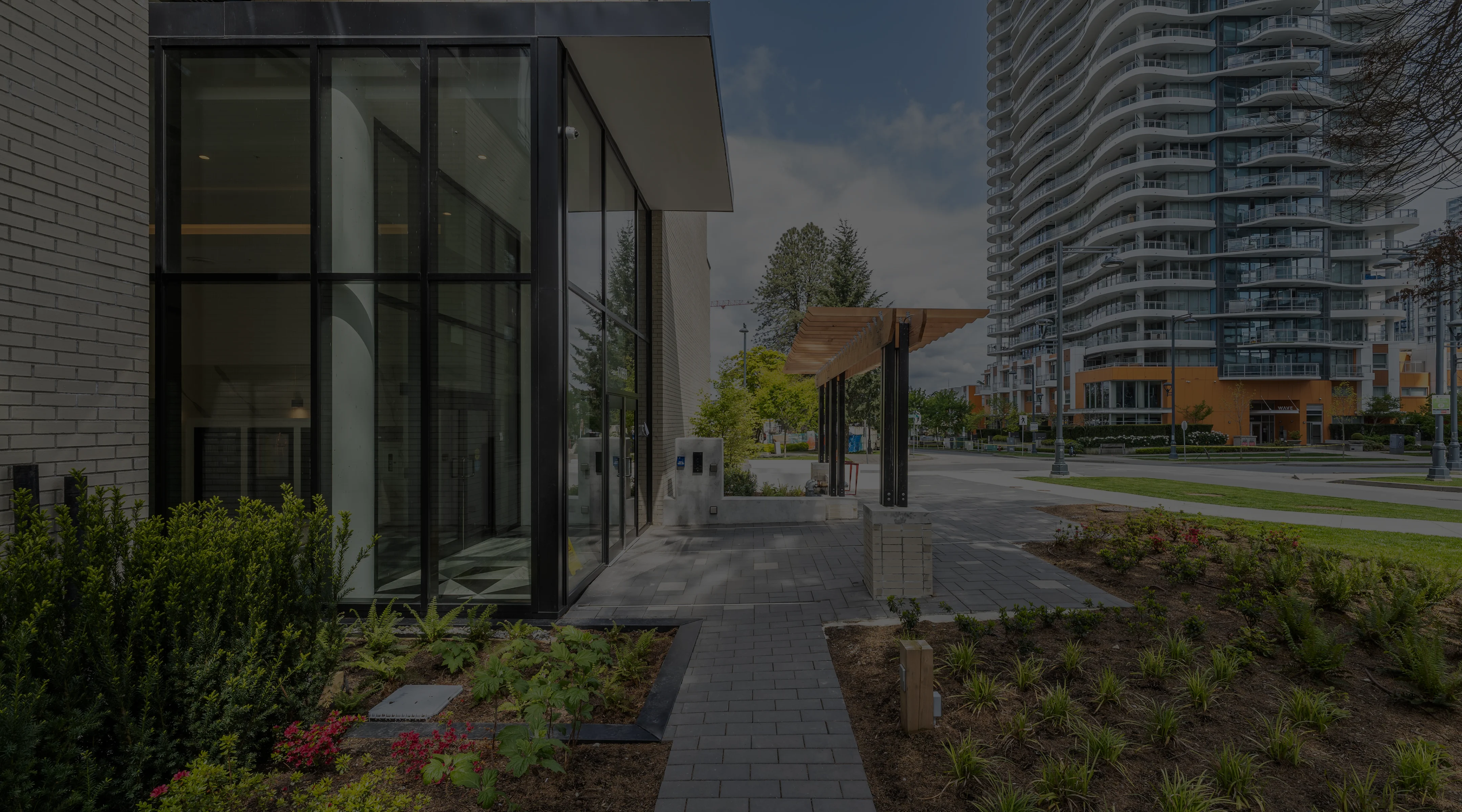 Paver walkway with planted beds beside a glass building entrance
