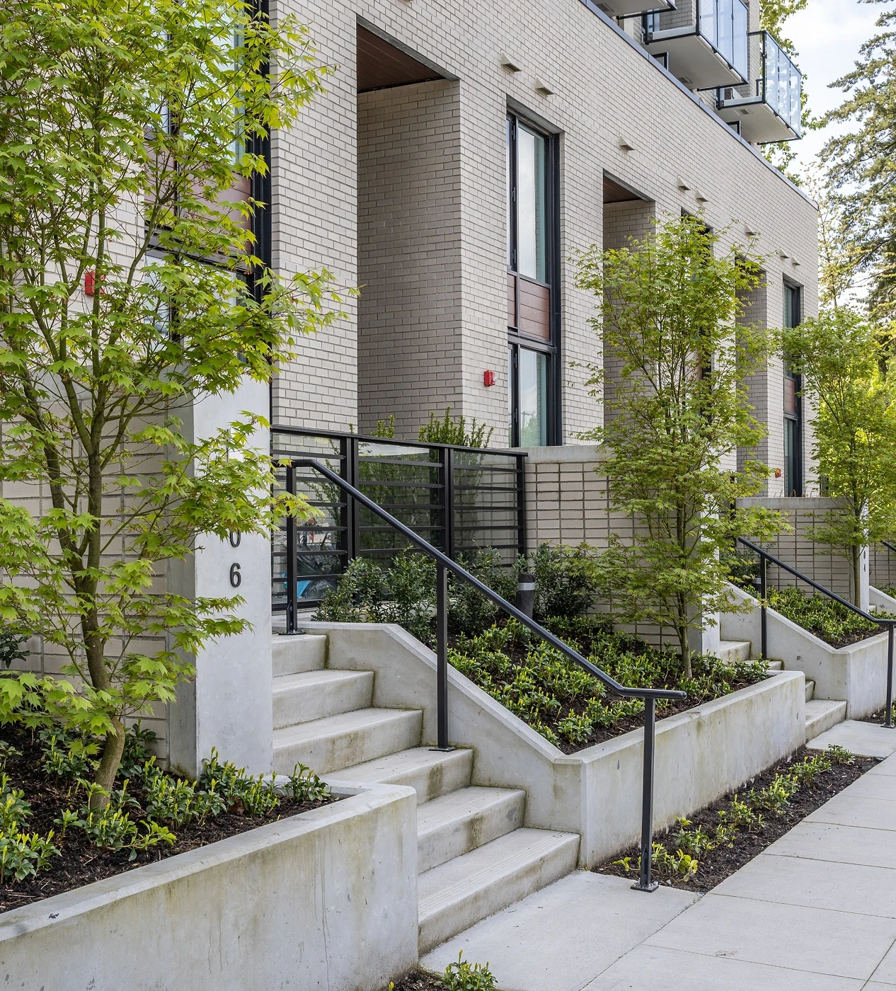 Concrete entry stairs with railings and planted beds at townhome entrances