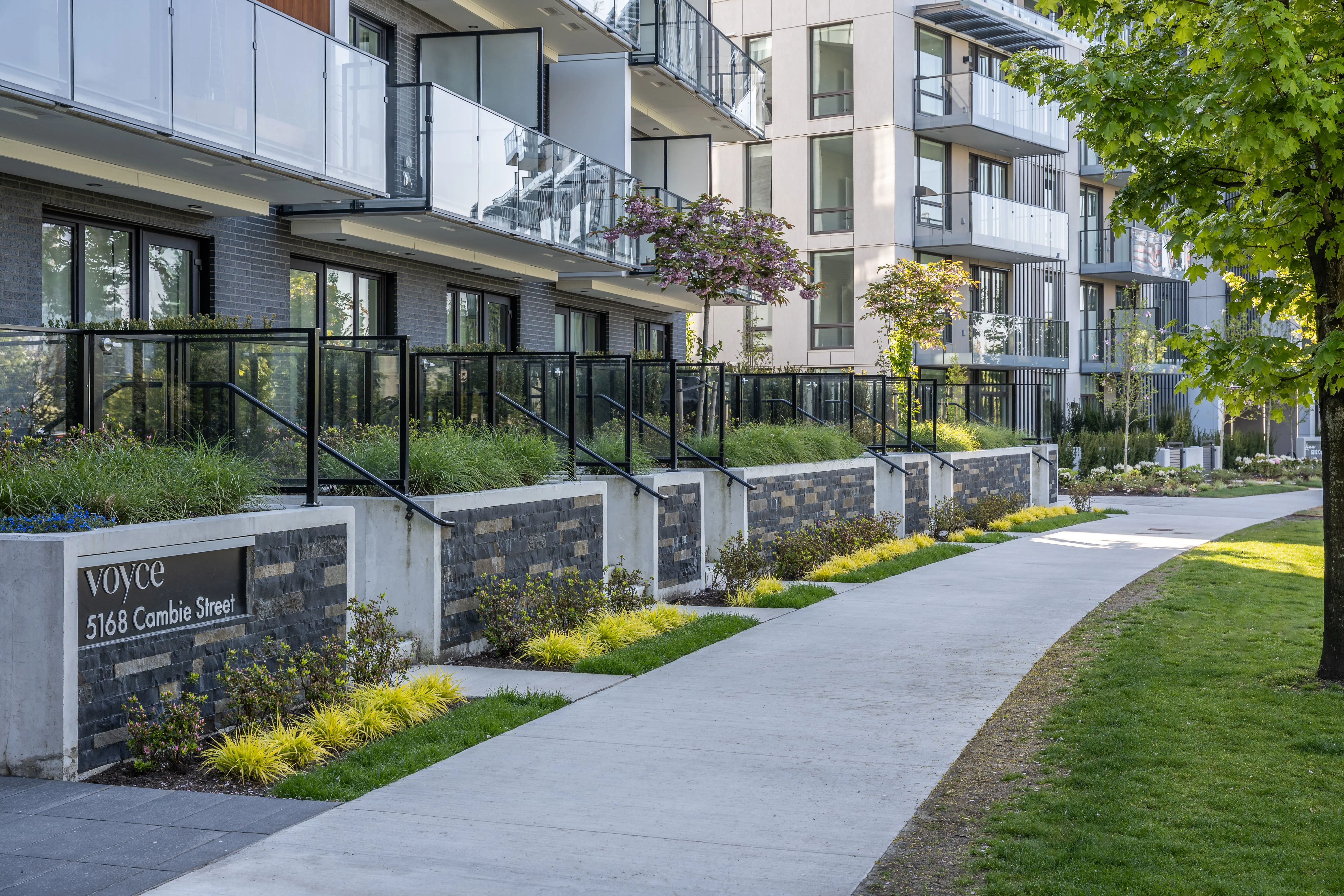 Building sign, lawn and planting along a sidewalk at Voyce